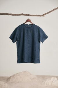 Home A fashionable dark blue shirt elegantly hangs from a branch against a minimal white backdrop.